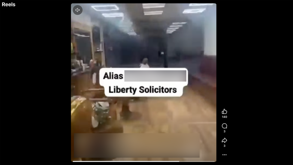 Ijtimoiy tarmoqdagi reel skrinshoti: yog‘och polli, stollar va stullar, shiftdagi yorqin chiroqlar bilan ofitseriya interyeri. Markazda katta matn: “Alias [redacted] Liberty Solicitors”. Video atrofida ijtimoiy tarmoq interfeysi elementlari ko‘rinadi: o‘ng tomonda layk, izoh va ulashish belgilari, pastda esa akkaunt ma’lumotlari va izoh matni. Video biroz xiralashgan, chap yuqori burchakda ovoz o‘chirilgan belgisi ko‘rsatilgan.