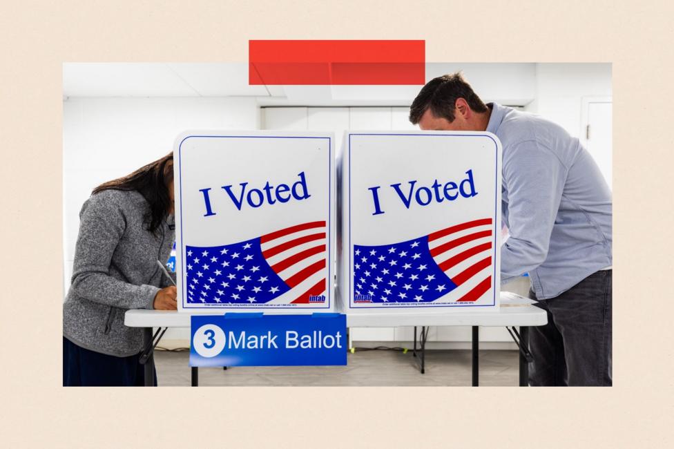 Two people cast their votes at a poll that has 'I Voted' printed on the side
