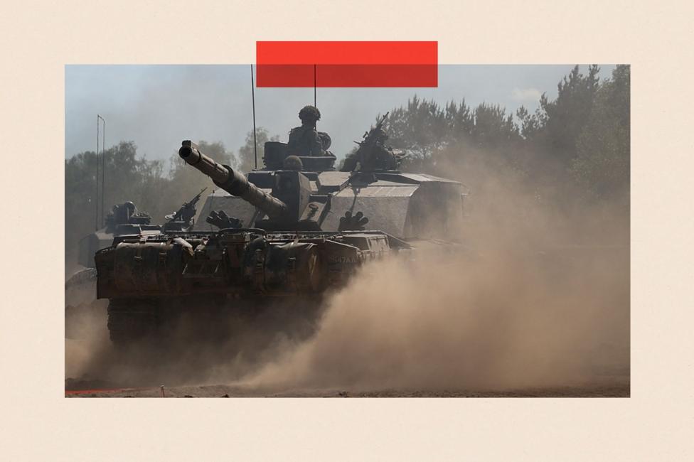 A tank on a dusty road with soldiers wearing helmets and military clothing seen riding the tank.