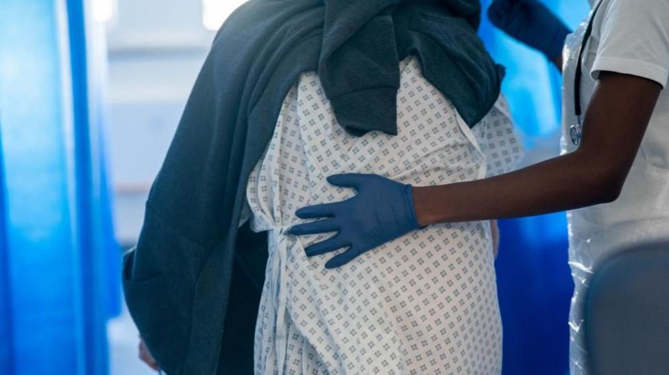 Rear view of a person in a hospital gown being guided by a healthcare professional