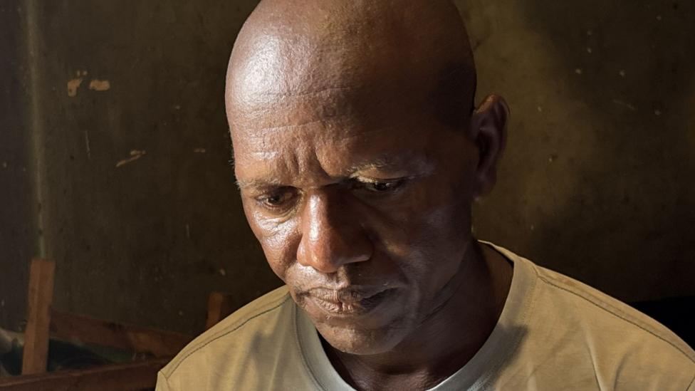 A close-up shot of a bald man wearing a white T-shirt looking down