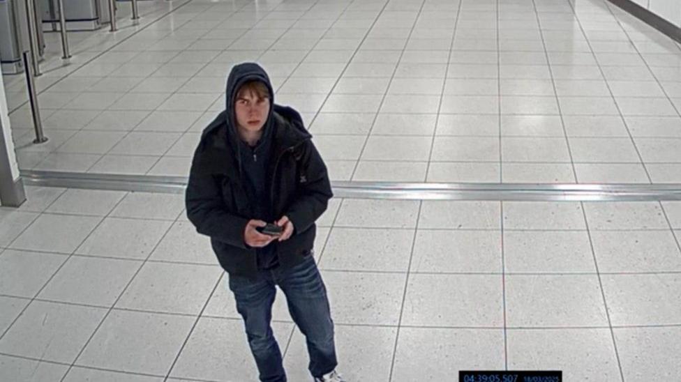 A CCTV image of a teenage boy wearing jeans and a hoodie at Manchester Airport