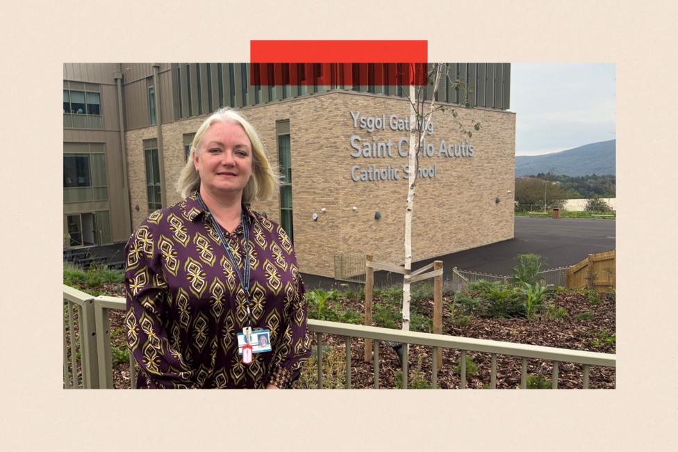 Sarah Hopkins stands in front of railings with the new school building in the background. She is wearing a purple and gold patterned top. The school is made of yellow brick and then higher up is what appears to be glass and metal