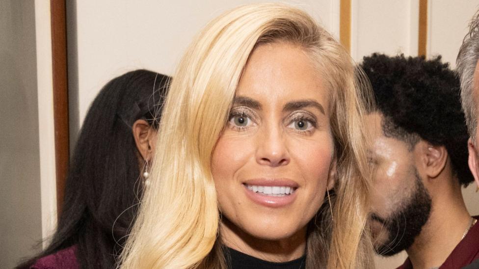 Woman with long blonde hair and pink lipstick and black turtleneck