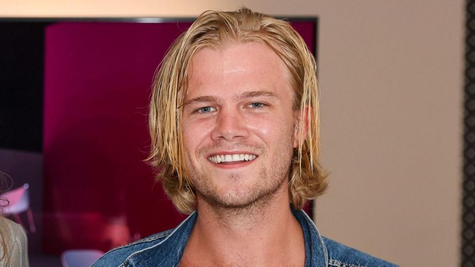 Chris Bourne, with blonde hair and a denim jacket, in 2021