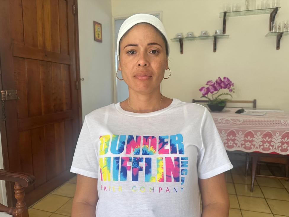 Heydi Sançez oşxonasida turgan holda kameraga qaragan, yorqin rangli futbolka kiygan