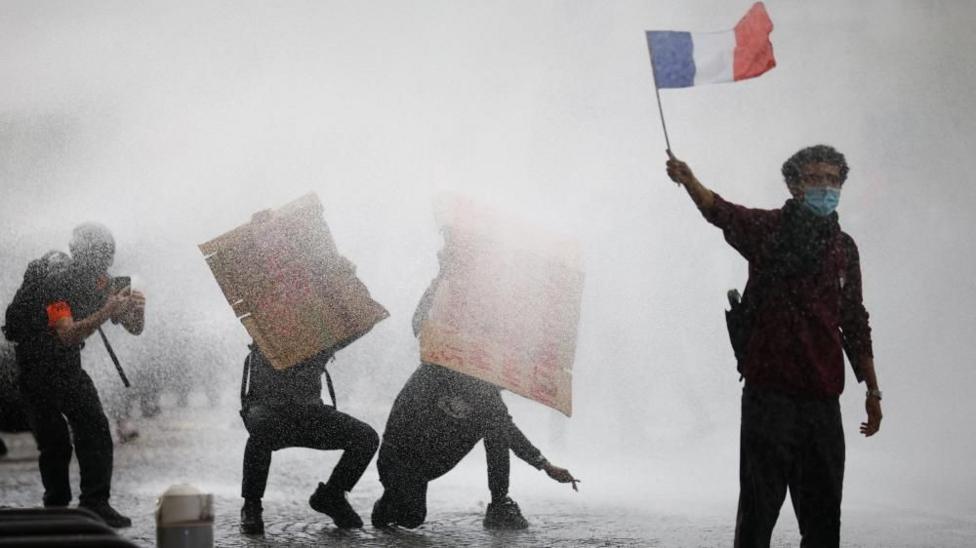 A masked protester holds a French flag as French police use a water canon amid clashes during a demonstration by French high school and university students in Paris.