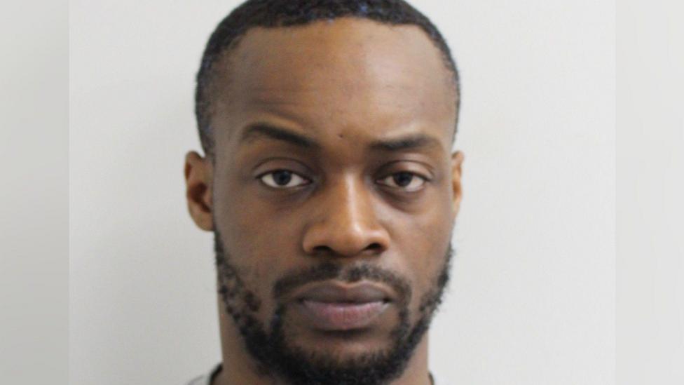 Gogoa Lois Tape, who has a small beard and very short hair, looks at the camera for a police custody photo 
