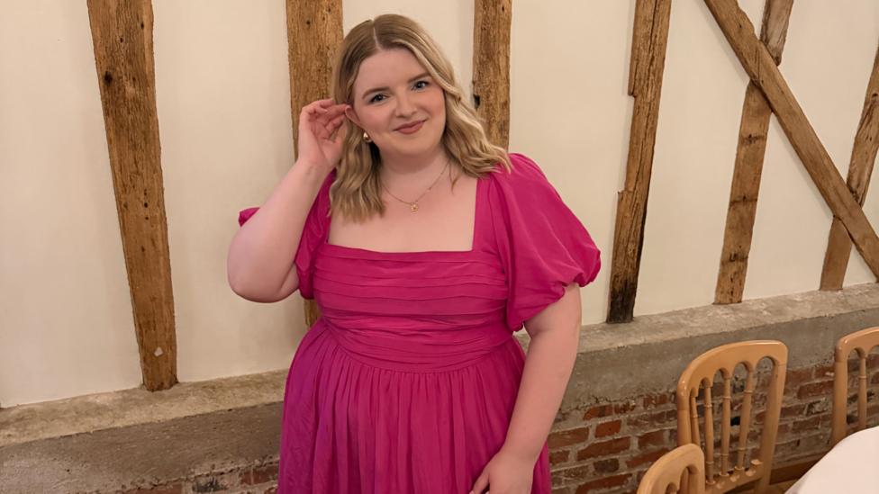 Jess is wearing a bright pink dress at a formal event. She has blonde wavy hair