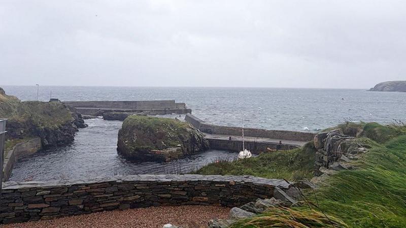 Port of Ness on the north coast of Lewis. There is a small boat sheltering in a harbour. The sky is cloudy.