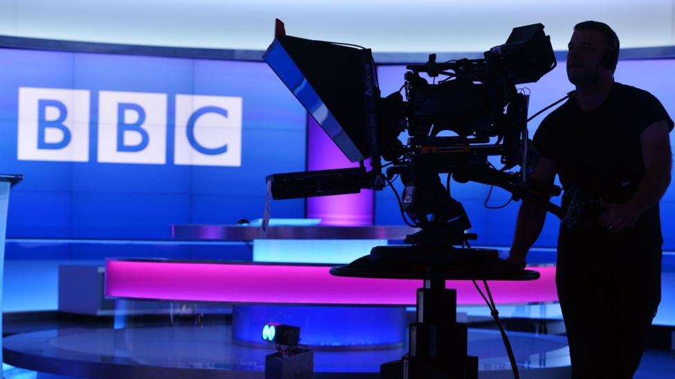 Studiyada operator, fonda BBC logotipi va pushti-binafsha fon ko'rinmoqda