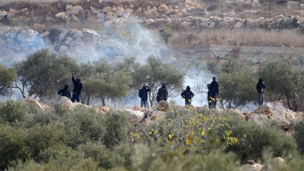 Israeli settlers stand near a fire amid clashes during olive harvest in Abu Falah near Ramallah