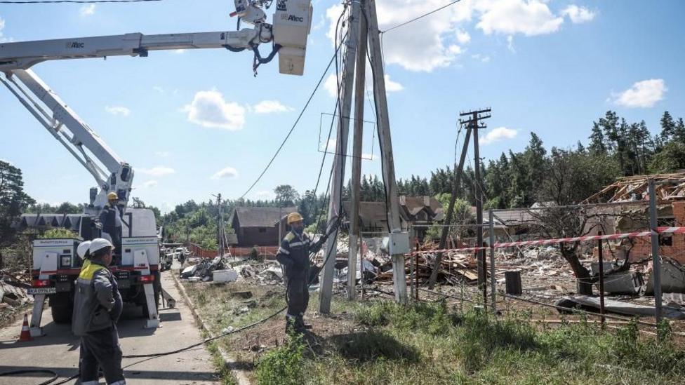 Energy workers stand beneath a power line as they work to restore supply following a strike