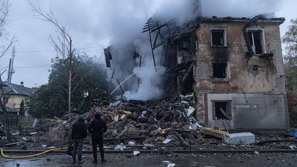 Two people stare up at the rubble of a residential building following a Russian guided-bomb attack in Sloviansk