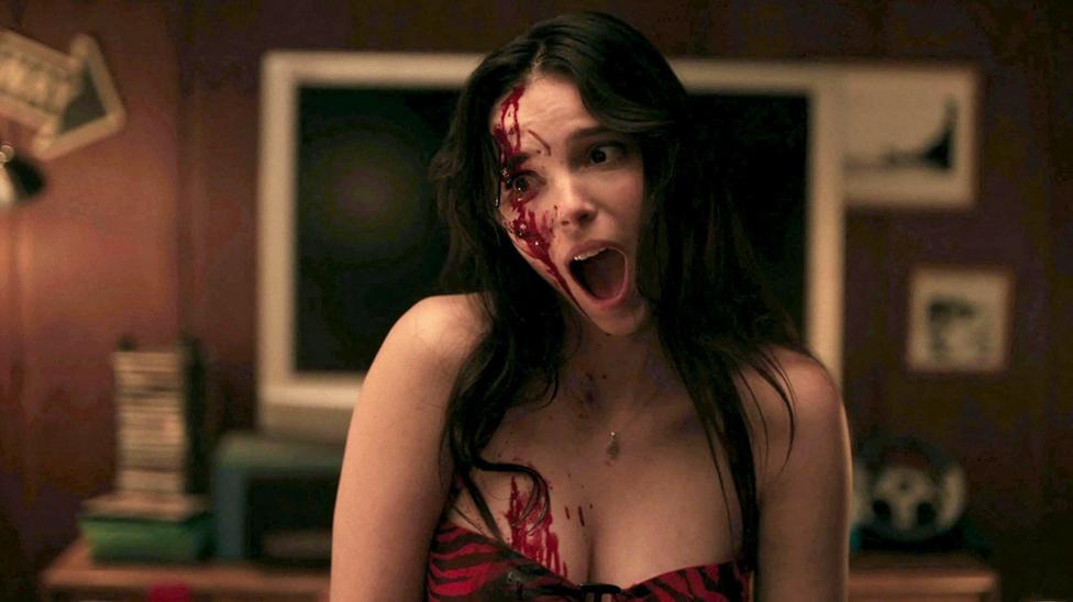 Inde Navarrette in Obsession looking to left of frame aghast with blood on her face, with her black-and-red zebra print dress just in view from an indoor scene from the film.