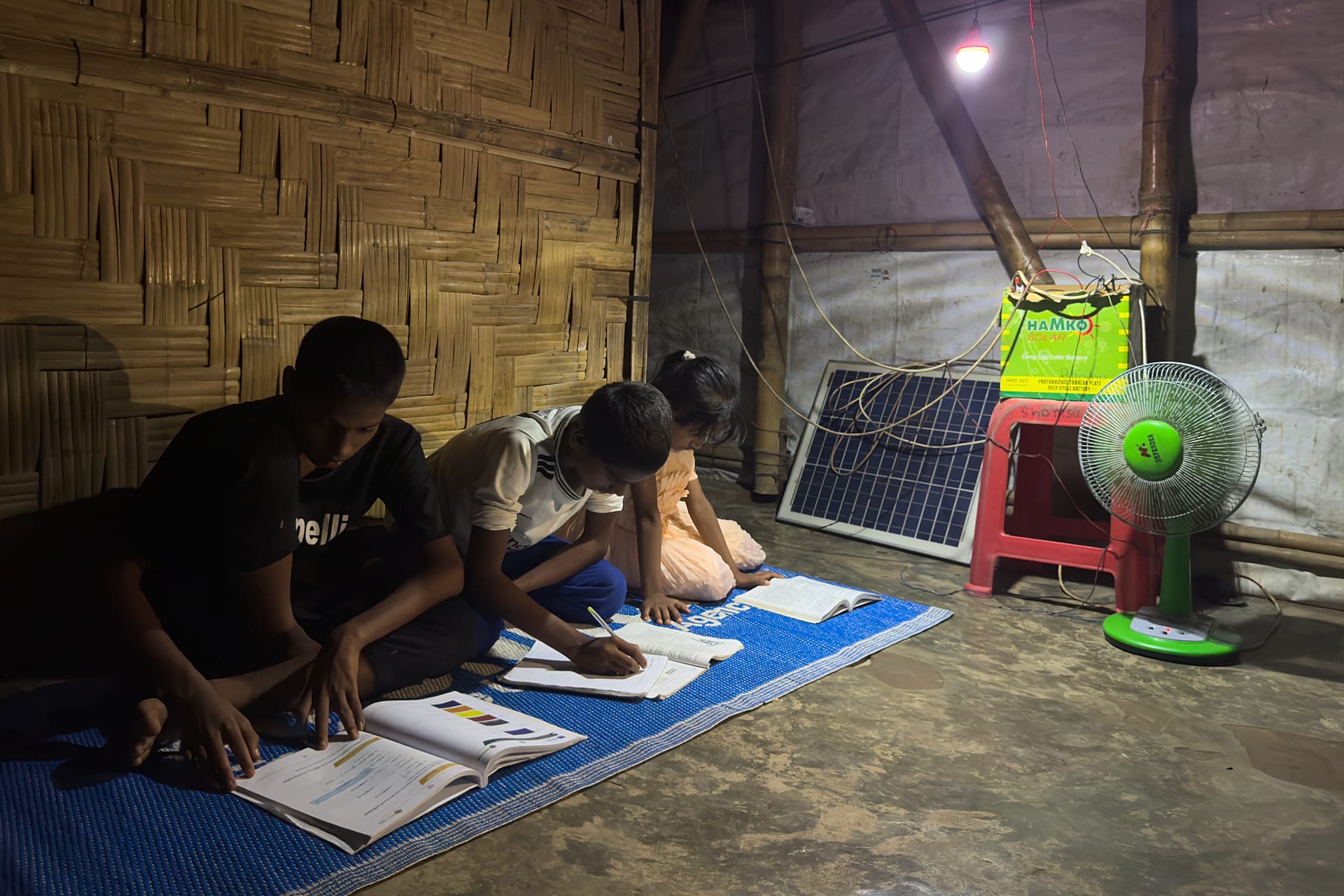 In this photo taken with a phone, children use a light powered by a solar panel to study at night inside their shelter on Oct. 3, 2026, in Teknaf, Bangaldesh.