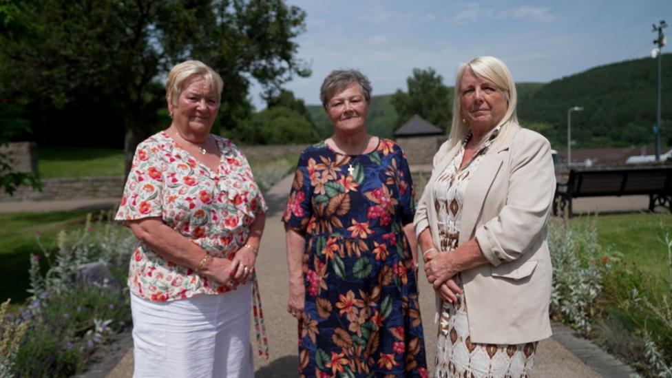 Three women standing in the sunshine in the Aberfan memorial garden on a sunny day