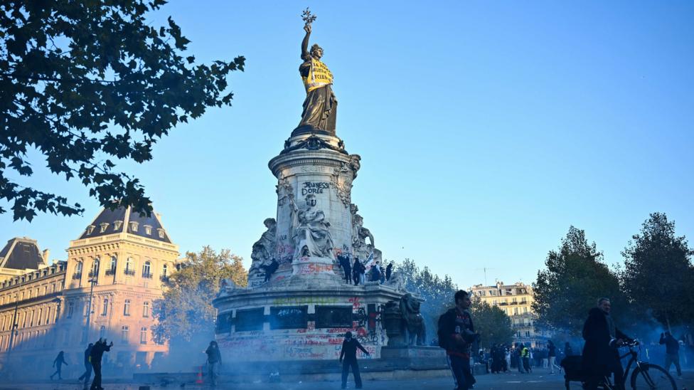 Protesters walk next to tear gas and the 'Statue de la Republique' as they gather as clashes erupted at Place de la Republique following a demonstration central Paris, on October 18, 2026.