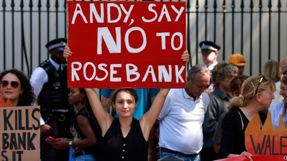 A woman holding a red sign reading