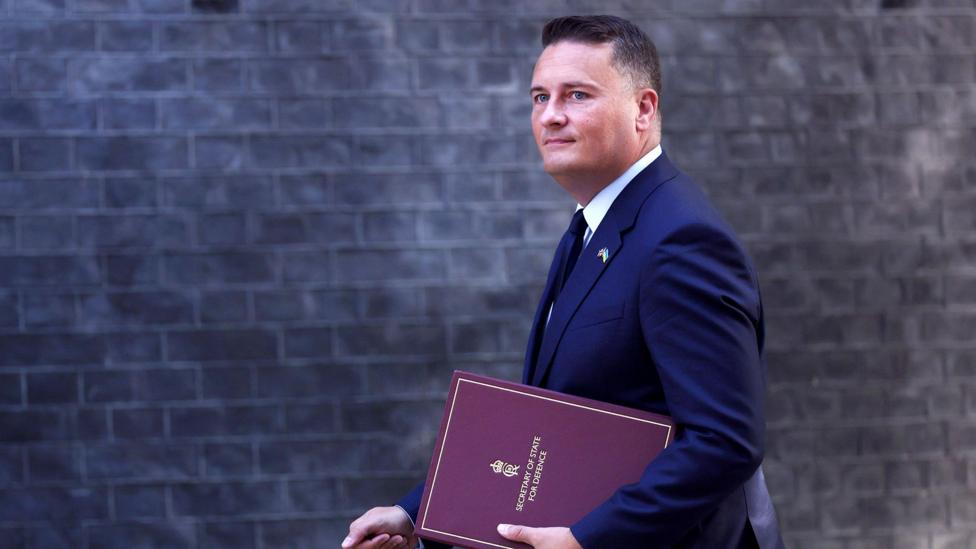 Wes Streeting sentyabr oyida Downing Street binosi fasadida oldinda, old tomonida 'Mudofaa vaziri' degan yozuv turgan papka bilan yurib bormoqda.