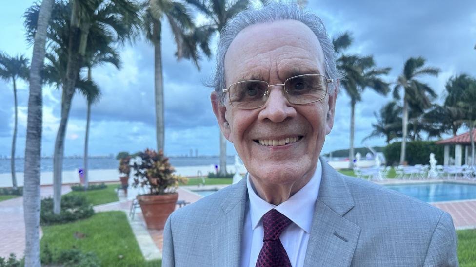 Juan Omar Sixto Floridadagi suziş havzasi va Biscayne körfazi oldida turgan. U kostyum va galstukda nafis kiyinib olgan