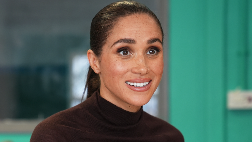 Head and shoulders of Meghan, Duchess of Sussex with a green background