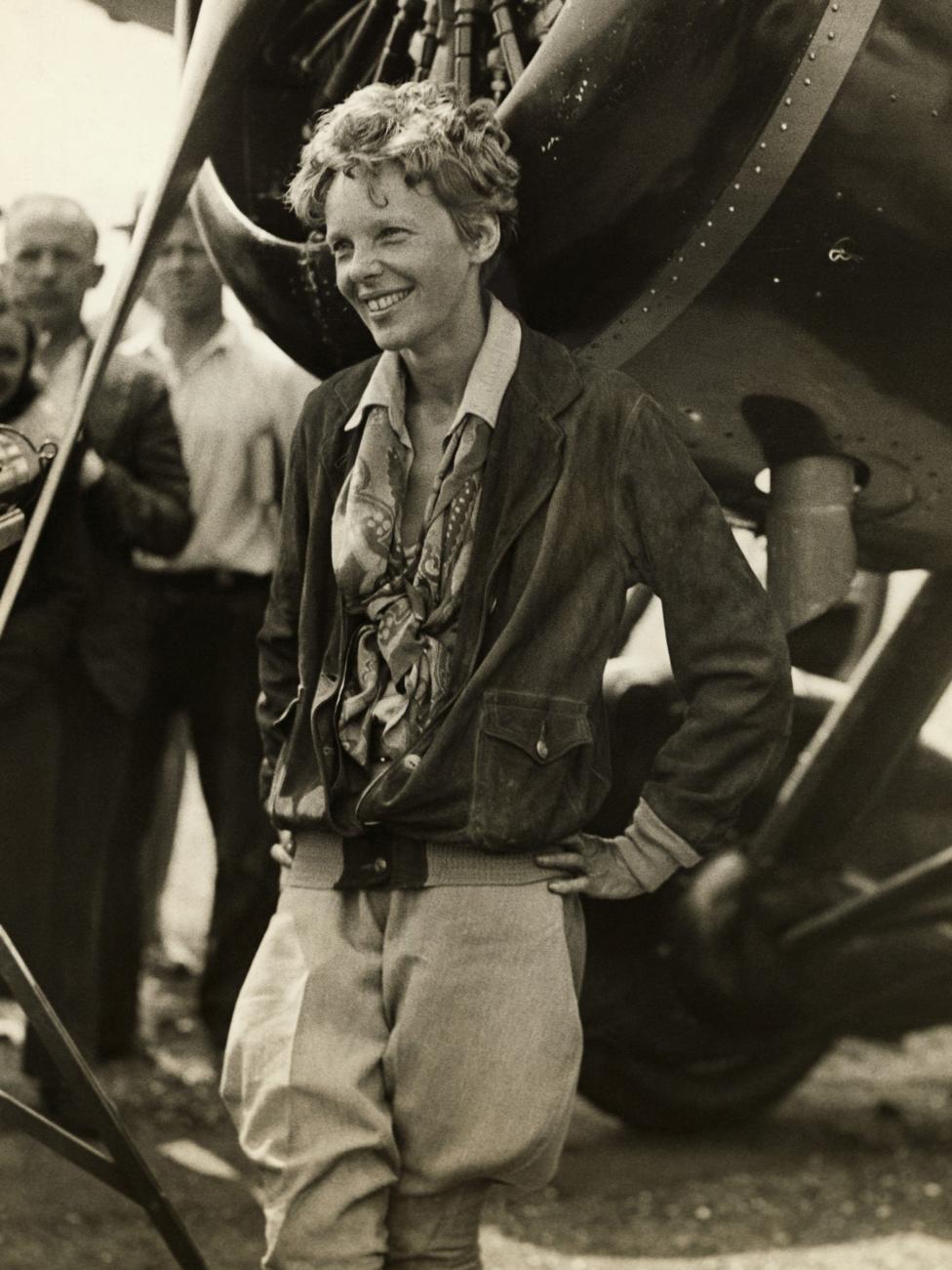 Amelia Earhart smiling as she stands near her plane, pictured in 1930.