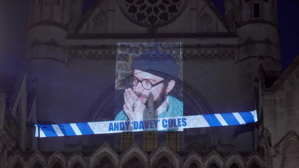A picture of Coles in a beanie hat is projected on to the central tower of the High Court building alongside a strip of blue and white police tape with