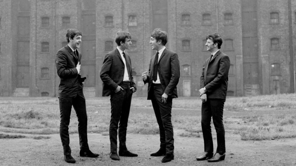 Black-and-white image of all four Beatles standing together in front of a large building during the band's early years.