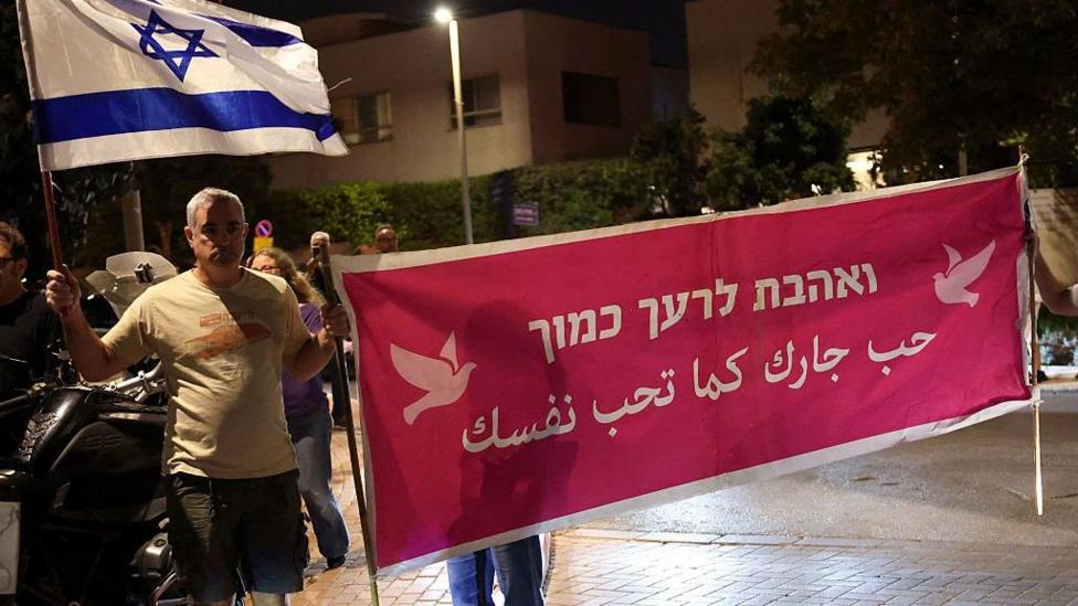 People demonstrate holding a banner that says 'Love your neighbour' in Arabic and Hebrew