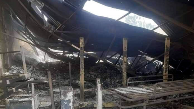 The ruins of a medical warehouse in el-Fasher, Sudan, showing a gaping hole in the corrugated iron ceiling and the shell of a gurney and other bits of furniture