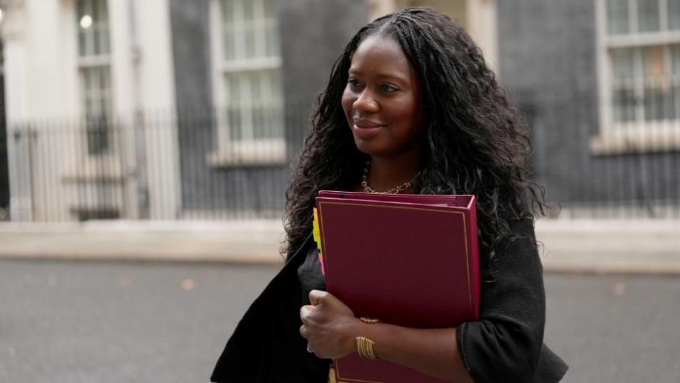 Miatta Fahnbulleh qizil papkani qo'lda ushlab, Downing Street bo'ylab yurmoqda.