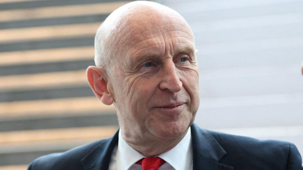 Head and shoulders of John Healey, wearing suit and red tie