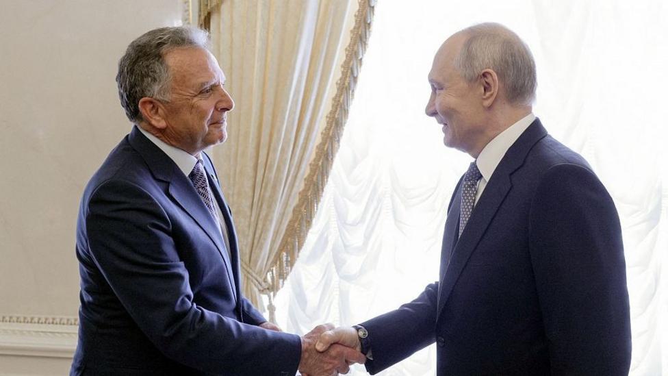 Президент России Владимир Путин пожимает руку спецпосланнику США Стиву Уиткоффу (слева). Оба в синих костюмах, улыбаются.