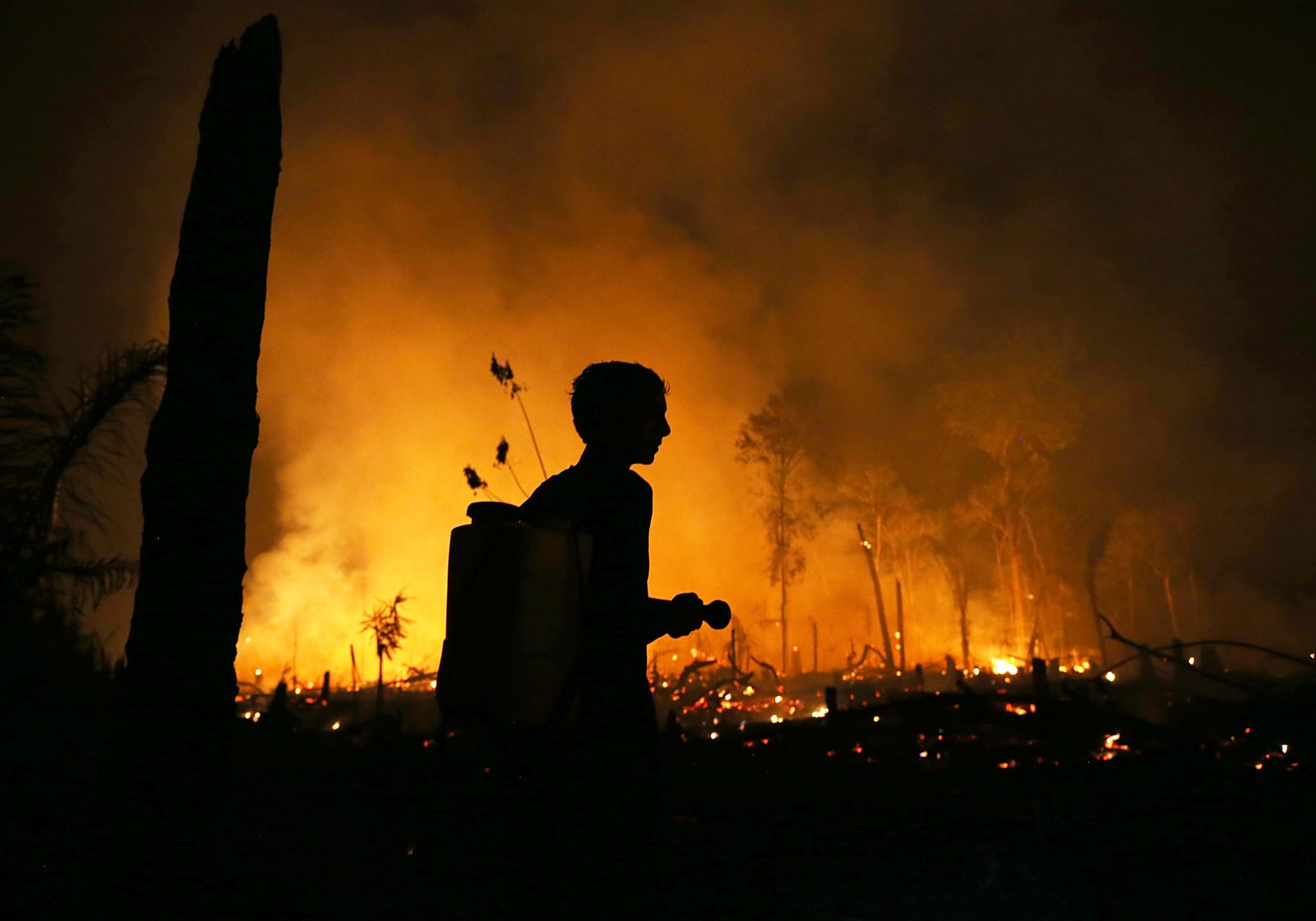 A resident with a flashlight looks at wildfires burning in the municipality of Autazes, Amazonas state, Brazil, Monday, Oct. 12, 2026.