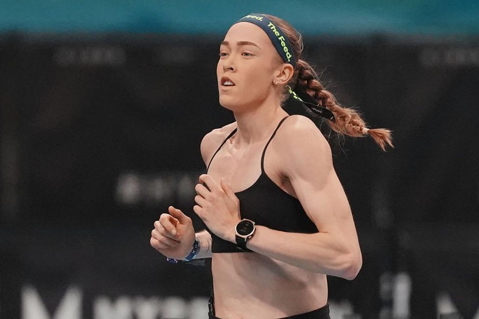 Joanna Wietrzyk qora sport brauzeri va 'the feed' sözlari yaşil harflar bilan bosilgan töqsiyoh tasma taqqan. Soçi örilgan, u yuguriş jarayonida.