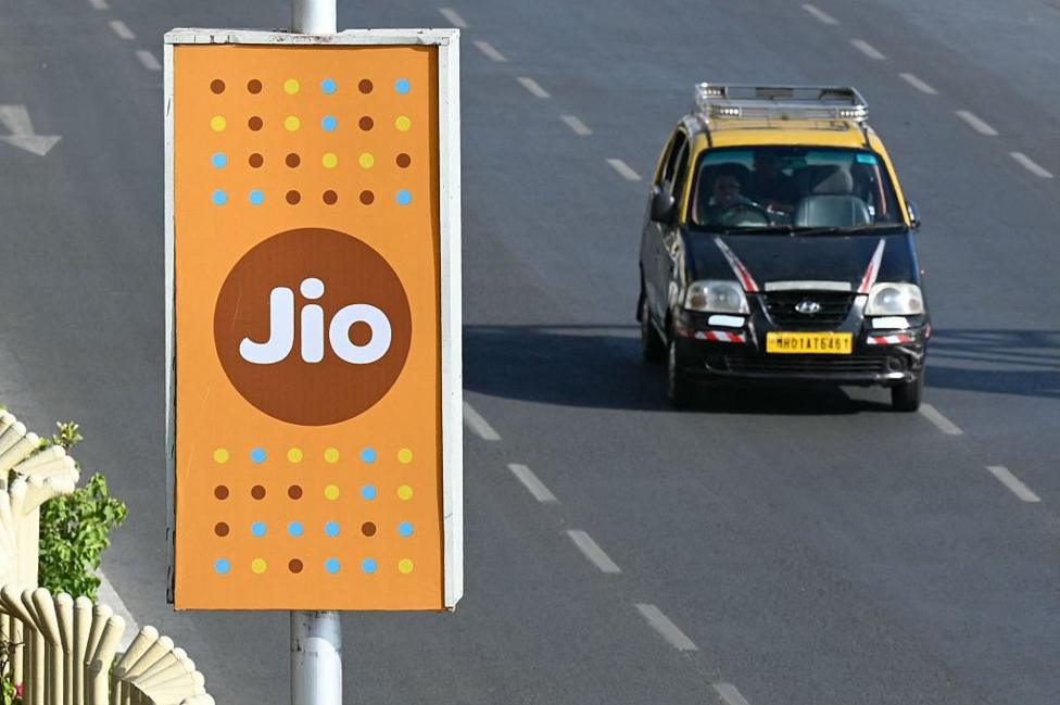 Такси чёрно-жёлтого цвета проезжает мимо рекламы Jio в Мумбаи.