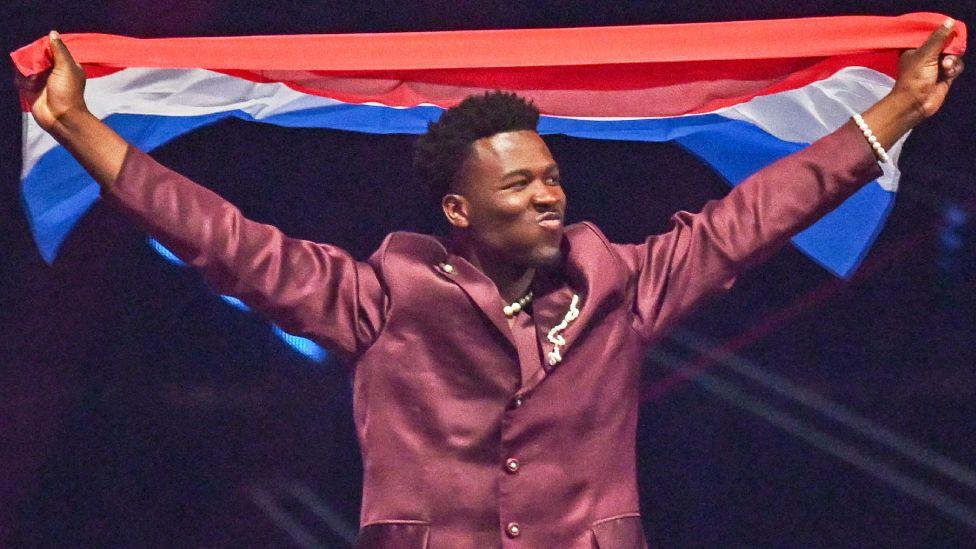 Нидерландский певец Клод, представляющий Нидерланды с песней «C'est La Vie», проходит с национальным флагом во время генеральной репетиции финала конкурса «Евровидение-2025» на арене «Санкт-Якобсхалле» в Базеле 16 мая 2025 года