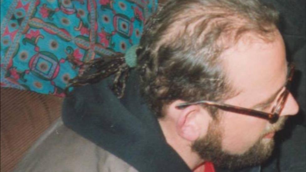 A rear side profile of Andrew Coles head. He has a short beard and is wearing round-rimmed spectacles. His long hair is tied back in a ponytail.
