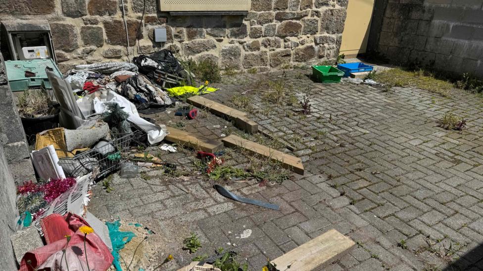 Rubbish is left on the driveway of a boarded up stone house