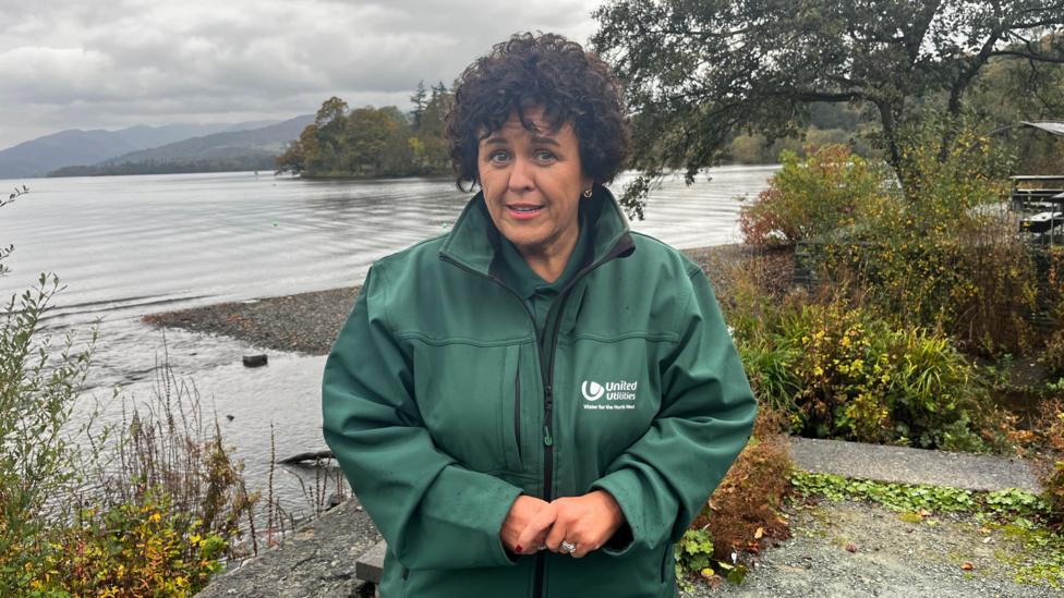 Louise Beardmore stands by the lake in a green jacket with United Utilities on.