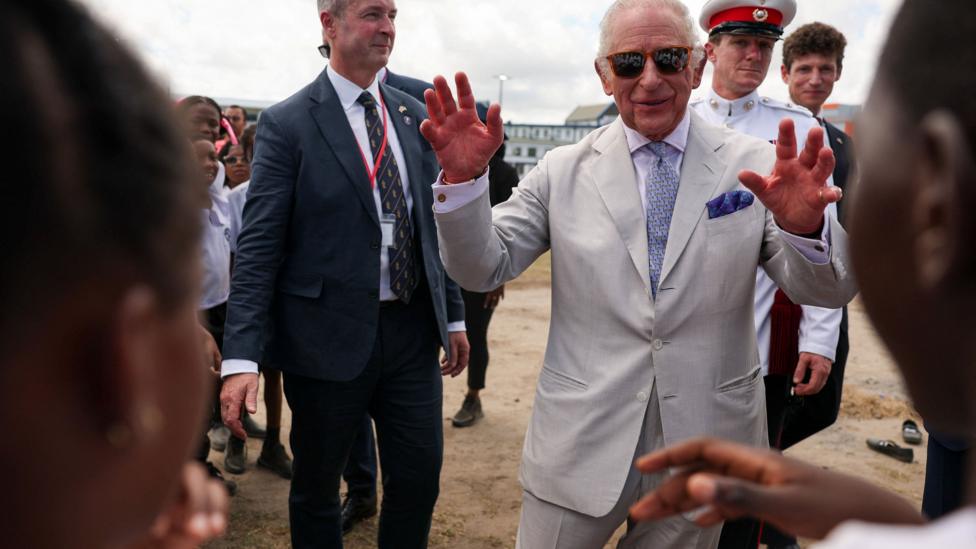 King Charles smiles and waves at young people in a public park