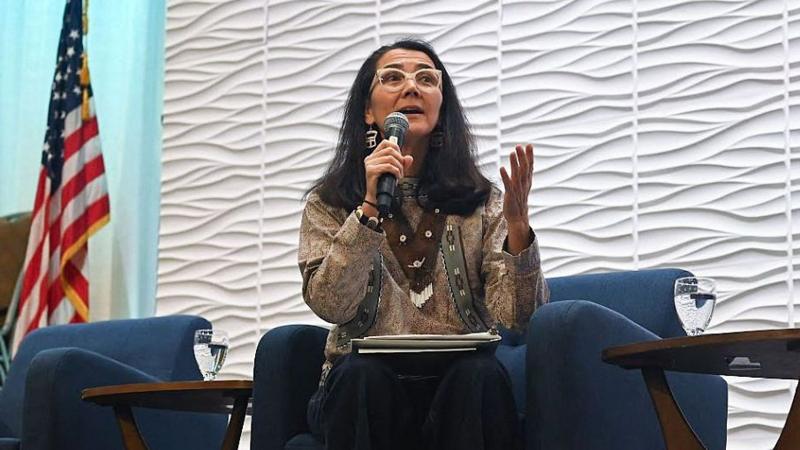 Mary Peltola holds a microphone and sits on a blue çair