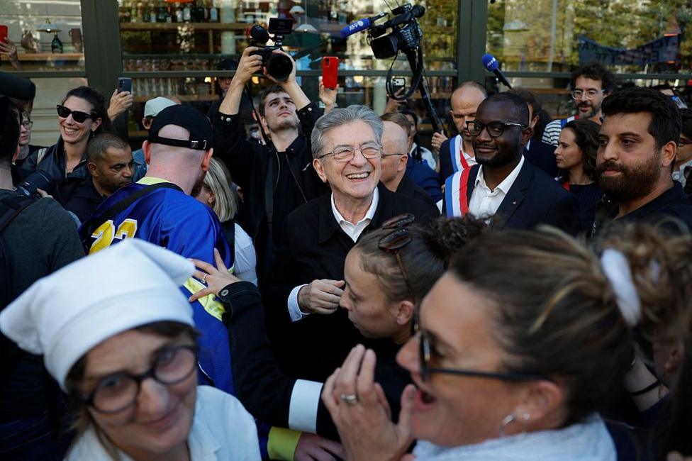 A man with grey hair grins whle surrounded by well-wishers