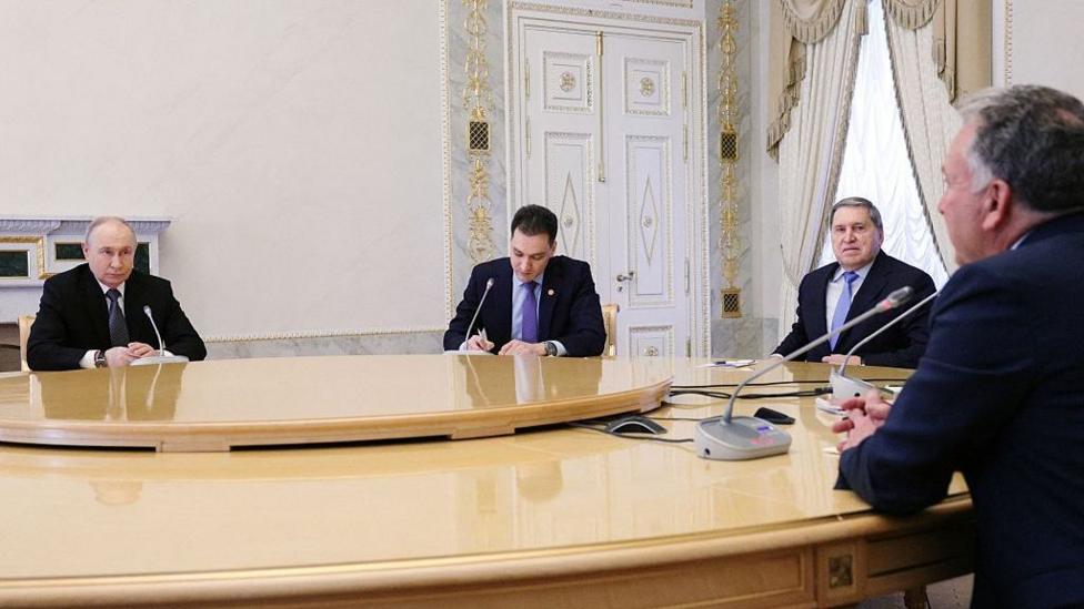 Vladimir Putin (L) sits at a large table with foreign policy aide Yuri Ushakov (second right), Steve Witkoff (R) and one other man
