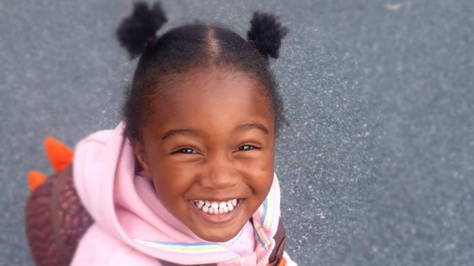 Zadie Ajetunmobi wearing a pink hoodie and smiling at the camera.