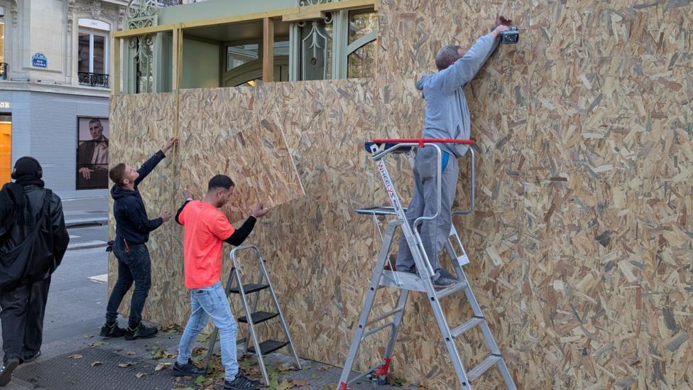 Three male workers, two on ladders, boarding up a shop front on the Champs-Elysees in Paris.