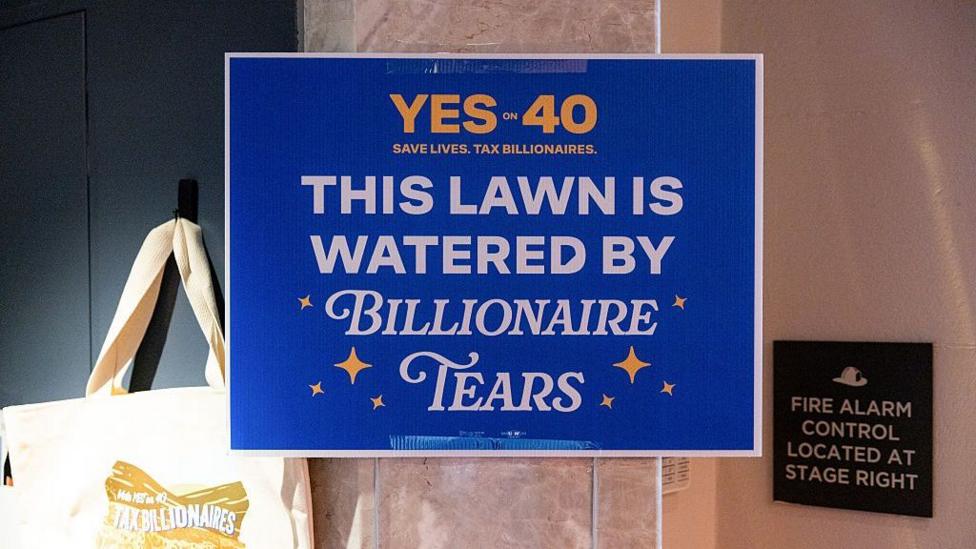 A 'Yes to 40 This Lawn Is Watered By Billionaire Tears' yard sign among merchandise for sale during a 'Yes on 40 for Ballots Over Billionaires' rally in San Francisco, California, US, on Saturday, Oct. 3, 2026.