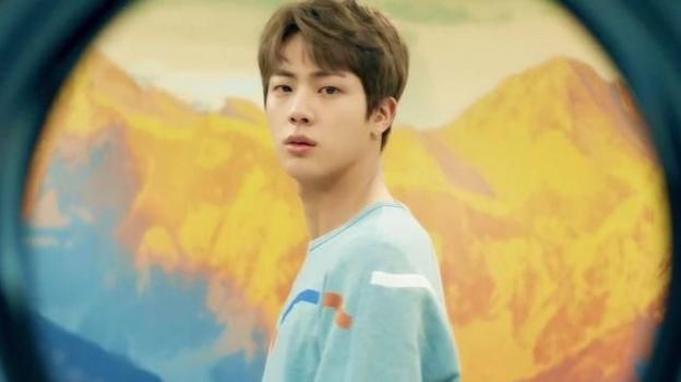 A K-pop star looks down the barrel of the camera, yellow tinged mountains behind him