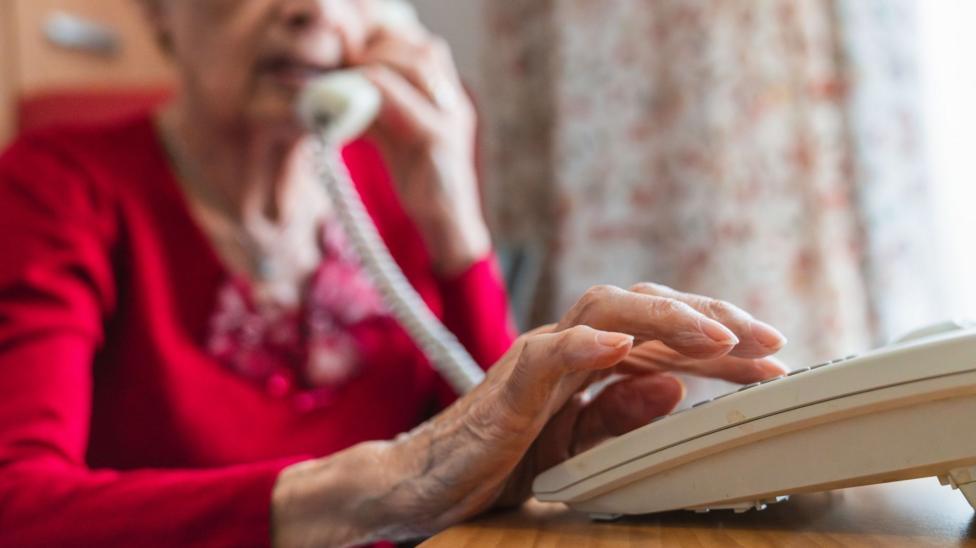 Qizil kardigan kiygan keksa ayol tugmali telefonda raqam termoqda